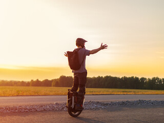 Man riding electric unicycle on road against sunset background. arms out to the sides, concept of travel and freedom © pavelkant