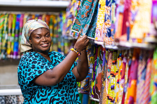 Smiling African woman, successful small business owner of an African Print, Ankara fabric shop proudly displaying textiles prints.