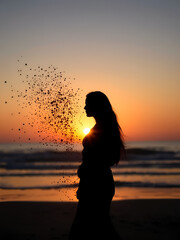 Fototapeta premium Silhouette of woman standing beach sunset. Particles disintegrate from form. Thoughtful. Tranquil scene evokes themes of change, transformation. Suggests inner journey. Seascape background shows calm