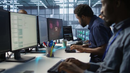 Programmer seeing red critical error popup on computer display in data center, panicking. African american man in server hub spamming keyboard buttons after receiving error, camera A