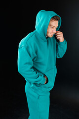 A fashionable man wearing an aqua hooded sweatshirt strikes a confident pose, exuding style as he...