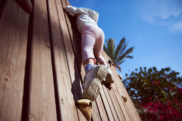Child Climbing a Wooden Wall Outdoors on a Sunny Day
