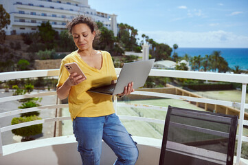 Woman Working Remotely Outdoors With Laptop and Smartphone On a Sunny Terrace Overlooking Palm...