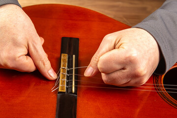 Close-up of hands restringing a red acoustic guitar, focusing on the bridge with new strings being...