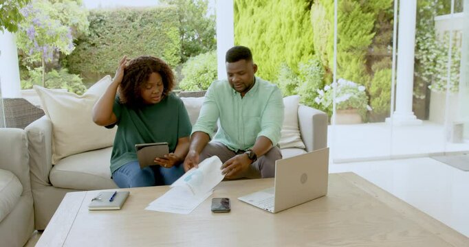 Mature couple reviewing documents and using laptop on patio, discussing finances