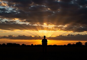 Silhouette gazing at sunset representing hope and reflection, with dramatic sky and golden light