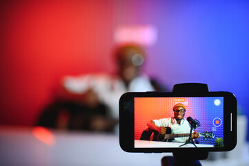 african american vlogger using smartphone to film podcast in studio. blogger with mobile phone,...