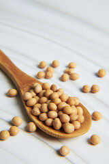 Soybeans piling up in wooden spoon on white table
