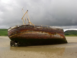Weathered Wooden Boat Stranded on Coastal Shore Beneath Stormy Skies