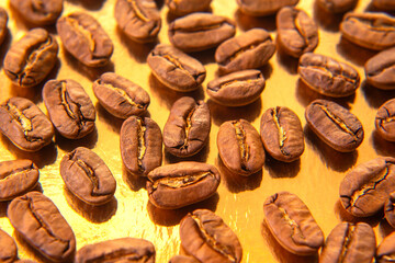 Roasted coffee beans in an oval shape on a reflective gold backdrop, displaying their warm brown...