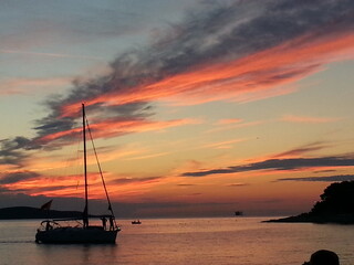 Stunning sunset: a lone sailboat silhouette drifts across serene waters beneath a kaleidoscopic sky...