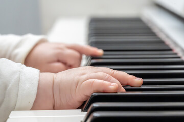 Obraz premium Super close-up of a baby's hand in a white sweater playing the piano in a bright setting. Young life and music.