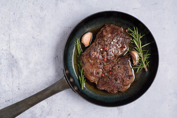 Fried Rib Eye steak with rosemary and garlic in a frying pan on a marble background. View from above.