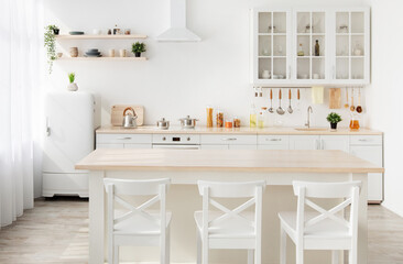 Style minimalism. Stylish kitchen in white and brown wood. Dining table, utensils and kitchenware on shelves, small white refrigerator near window