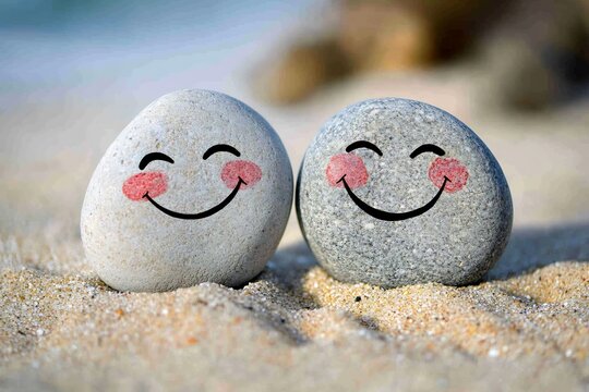 Two pebbles painted smiling faces on a sandy beach symbol of playful and light hearted friendship