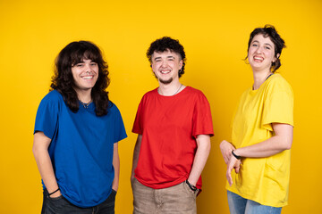 Three happy young adults smiling on yellow background