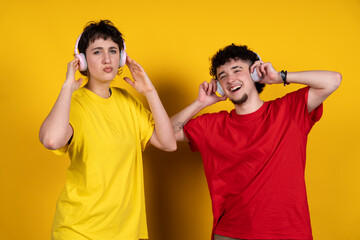 Young people enjoying music with headphones on yellow background