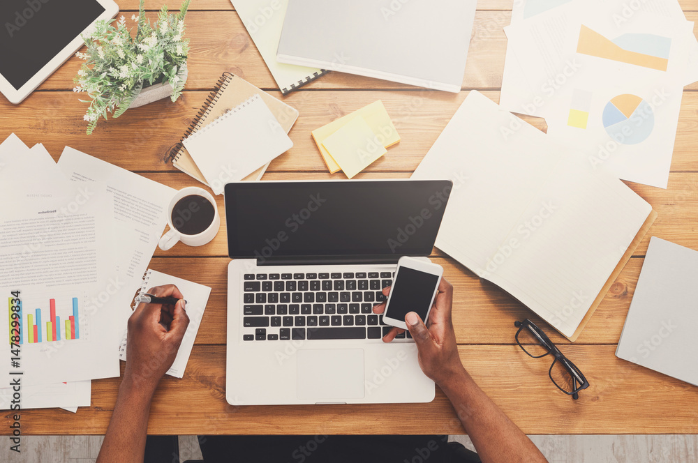 Poster office workspace top view. african-american businessman working at wooden desk, using laptop and var