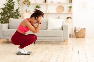 Fototapeta premium Unsuccessful Diet. Desperate African Girl Shouting Standing On Weight-Scales Trying To Slim At Home. Free Space