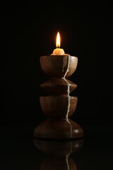 Burning candle in candlestick on mirror surface against black background