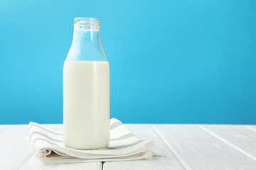 Fresh milk in glass bottle on white wooden table against light blue background. Space for text