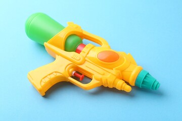 Bright plastic water gun on light blue background, closeup