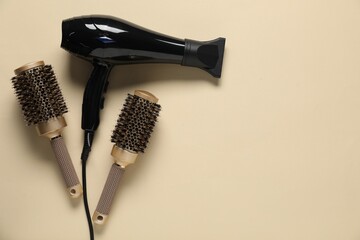 Round brushes and dryer on beige background, flat lay. Space for text