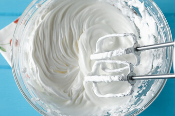 Whisking cream with hand mixer at light blue table, top view
