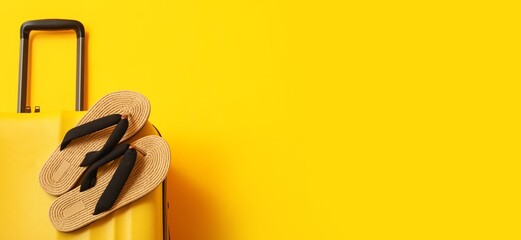 Suitcase and flip-flops on yellow background with space for text, closeup. Tourism concept