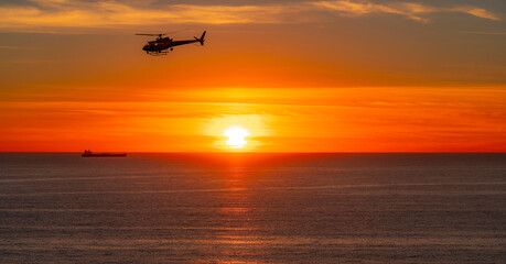 Helicopter crosses over ocean during dramatic orange sky 