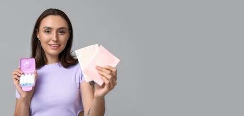 Beautiful young woman with tampons and menstrual pads on grey background with space for text