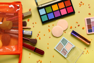 Stylish red cosmetic bag with makeup products on yellow background