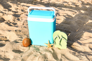 Modern beach cooler, flip-flops and ripe coconut on sand