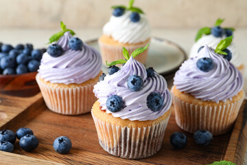 Wooden board of delicious cupcakes with blueberries and mint on white background