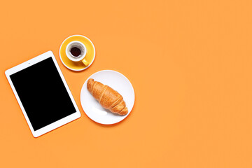 Tablet computer with blank screen, cup of coffee and croissant on orange background