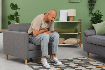Fototapeta premium Young man with appendicitis sitting in armchair at home