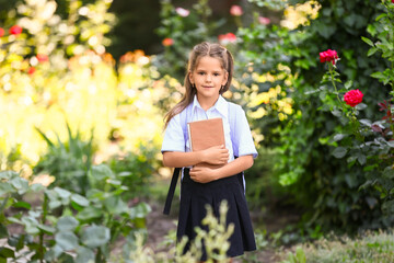 Fototapeta premium Little schoolgirl with backpack and book outdoors