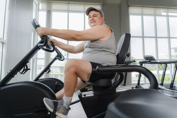 Fototapeta premium A middle-aged, overweight man uses a bicycle to exercise at the gym.