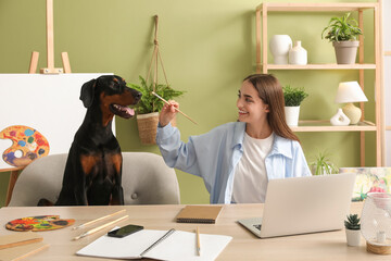 Cute Doberman dog and beautiful young happy woman with paints palettes working at home