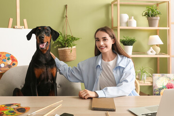 Cute Doberman dog and beautiful young happy woman with paints palettes working at home