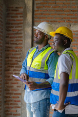 An African male engineer is overseeing the construction of a building with construction workers who are checking and planning the work on his tablet.