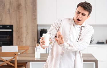 Young man rejecting glass of milk in kitchen
