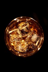 Overhead shot of whiskey on the rocks in glass on black background showing ice cubes and condensation in studio