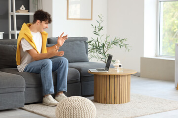 Obraz premium Young man video chatting with laptop on sofa at home