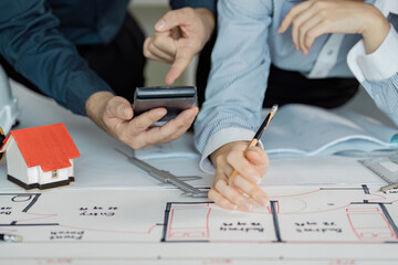 Engineers reviewing architectural plans and calculations with tools and a model house.