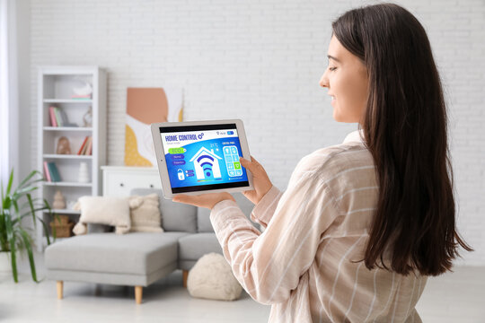 Young woman with smart home security system control panel in room, back view