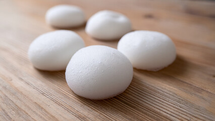 Close-up shot of fluffy white cleansing foam dollops placed on a light wooden surface, giving a fresh, clean, and approachable vibe, soft morning light, no branding elements.