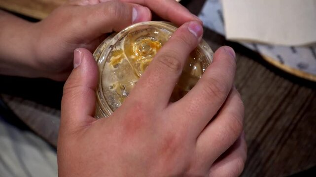 Close-up video of iced coffee being stirred with a straw, ice cubes swirling, followed by closing the plastic lid. A refreshing and satisfying drink preparation scene.

