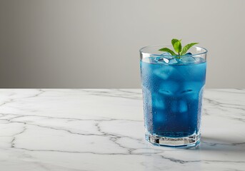 A refreshing blue cocktail with ice cubes and a mint leaf, served in a tall glass on a marble countertop.