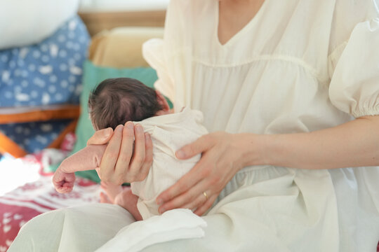 A Japanese mother in her twenties holds her 7-day-old newborn baby on her shoulder, burping the baby while sitting on a sofa. This photo shows the love shared in the early days of motherhood.